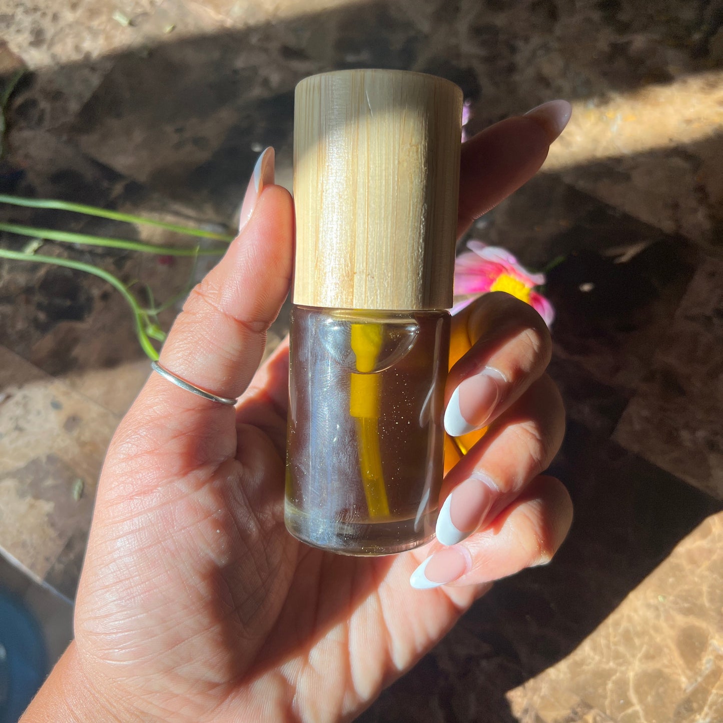 Hand holding a small glass bottle with a wooden cap against a natural background
